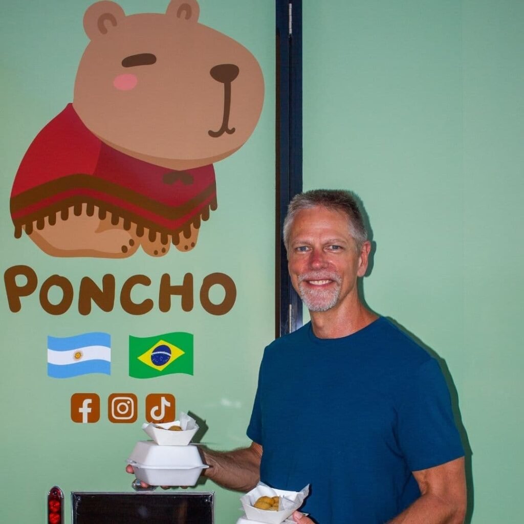 Customer holding a drink posing next to the capybara logo on the truck.