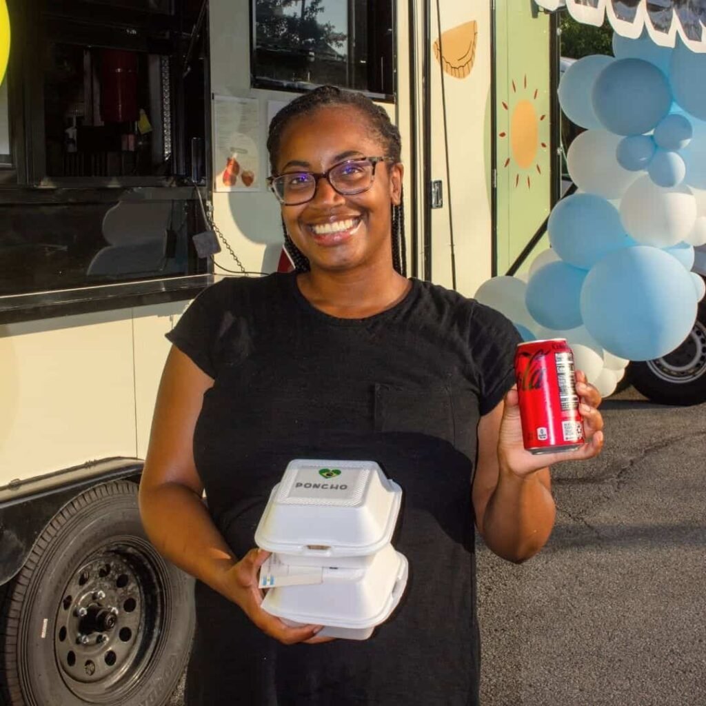 Woman holding takeout containers and a drink near the food truck.