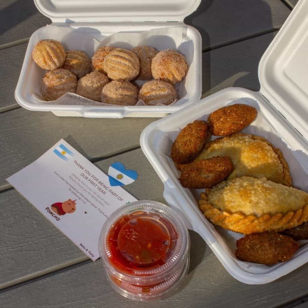 Takeout containers filled with empanadas and dipping sauces.
